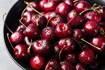 Fresh ripe black cherries in a black bowl Grey background