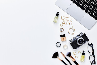 Various beauty products with camera and laptop on white background