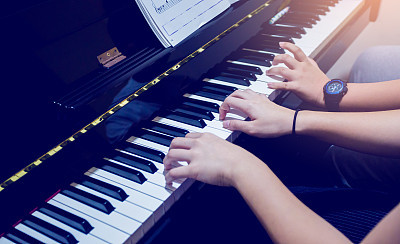 Selective focus to picture of young woman teaching a boy to play the piano with music notation.