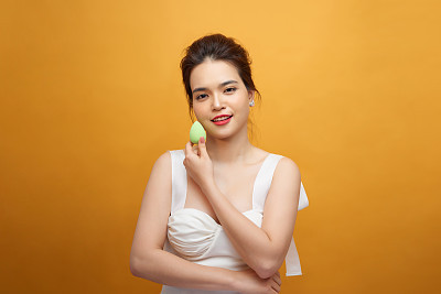 Asian woman using beauty sponge blender over yellow background