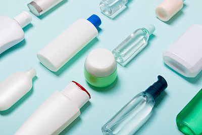 Close-up set of diffrent sized bottles and jars for cosmetic products on blue backgound. Face and body care concept with copy space