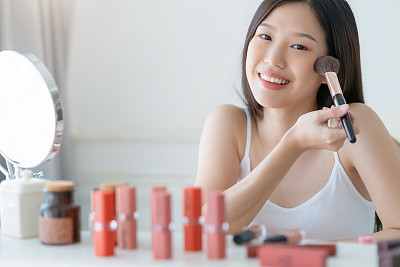 beautiful asian woman white tshirt smile with happiness hand hold blush on and makeup cosmetic items in bedroom with healthy  face skincare concept
