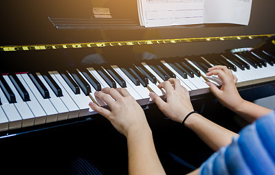 Selective focus to picture of young woman teaching a boy to play the piano with music notation.