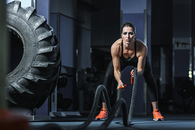 Powerful attractive muscular Fitness trainer do battle workout with ropes