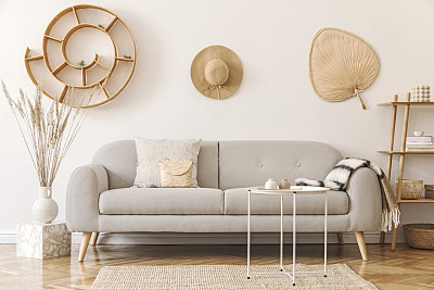 Stylish and cozy interior of living room with a lot of rattan accessories, design gray sofa and wooden shelf. Korean style of home decor. Hanging rattan snail with airplants, hat and leaf. Template.