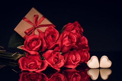 Red roses, gift and heart shaped chocolate on black background