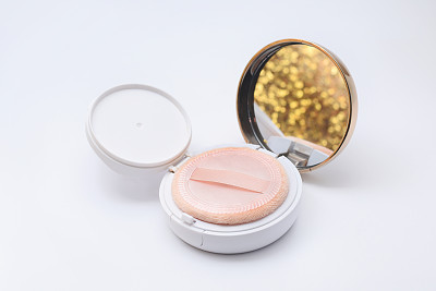 foundation powder cushion with beige puff and shining golden reflection on white background