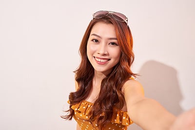 Carefree, careless concept. Young girl take selfie on front camera of modern smartphone wear in summer dress and beaming toothy smile isolated on shine beige background