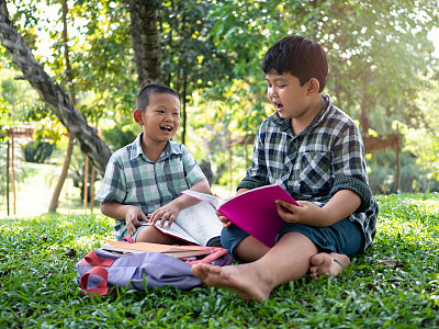 Cute two asian student boy reading book in the nature park with sunlight  background, people, learning, relax, education and Natural classroom concept