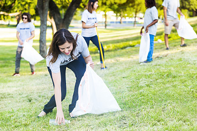Woman bends down to pick up trash in park