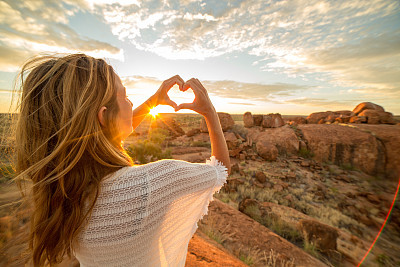 Young woman makes heart shape finger frame to spectacular landscape-sunrise