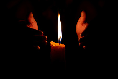 Candle burning fire flame and hand protect it on black dark background