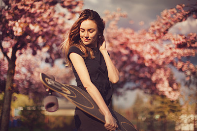 Young woman with longboard in cherry blossom alley