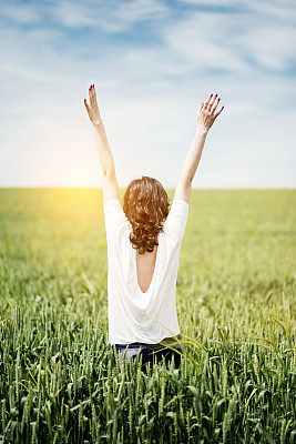 Young woman at sunset spreading arms in a field of grass