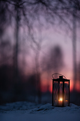 Lantern in snow against defocused sunset forest background.