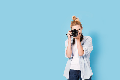 Young blonde photographer is taking a photo. Model isolated on a blue background with copy space
