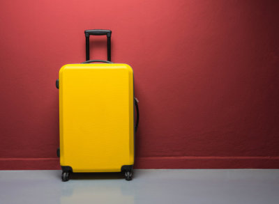 Yellow suitcase with extended handle against red wall