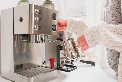 Woman steaming milk for cappuccino on professional espresso machine