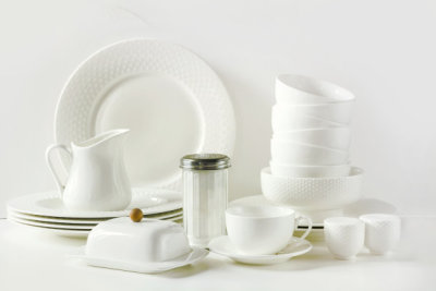White tableware for serving. Crockery,dish, utensils and other different white stuff on white table-top. Kitchen still life as background. Copy space.