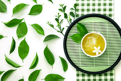 Top view shot of a hot cup of tea with green leaf decoration  with green napkin on white background , Organic green Tea ceremony time concept