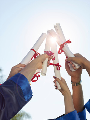 Group of college graduates holding diplomas in air
