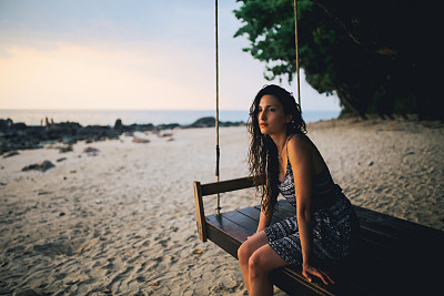 Young brunette woman on the beach of Koh Lanta island, Thailand, relaxing in the swing