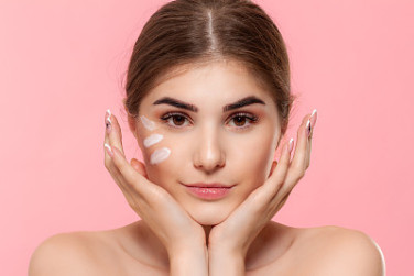 Beautiful model looks at the camera while moisturizing cream with hyaluronic acid is applyed to her skin.