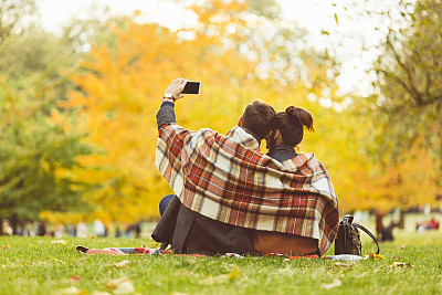 Back view of couple taking selfie at public park on autumn weekend