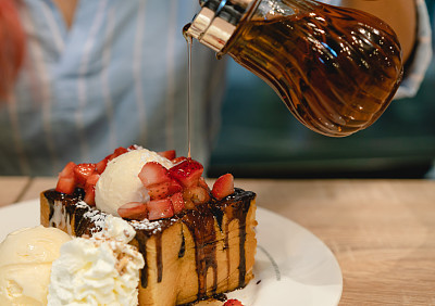 Woman pouring sweet maple syrup over Japanese Brick Toast dessert in trendy cafe