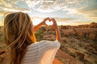 Girl makes heart shape finger frame to spectacular landscape-sunrise