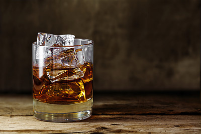 glass scotch whiskey with ice on a rustic wooden table