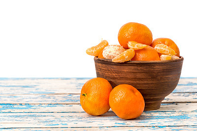 Bowl with tangerines on the old blue wooden table. Isolated on white.