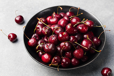 Fresh ripe black cherries in a black bowl Grey background