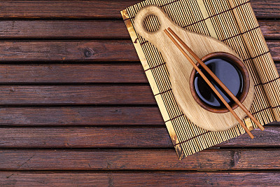 Background for sushi. Bamboo mat, soy sauce, chopsticks on wooden table. Top view with copy space