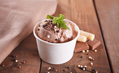 Paper bowl of chocolate ice cream, waffle cone and spoon for ice cream on wooden background.