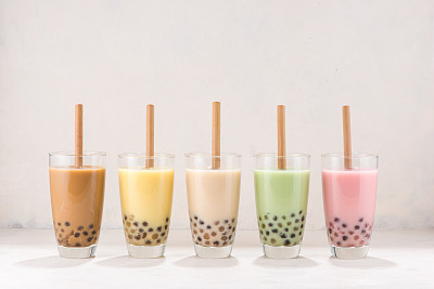 Row of fresh boba bubble tea glasses with straw on white background.