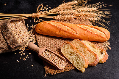 Fresh fragrant bread with grains and cones of wheat against a dark background. Assortment of baked bread on wooden table background
