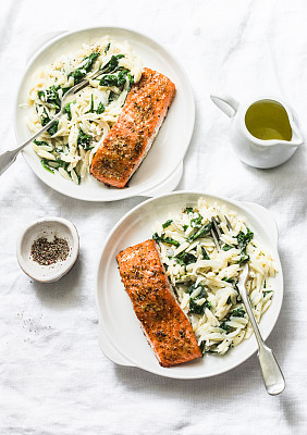 Healthy balanced lunch - creamy spinach orzotto and baked salmon on a light background, top view