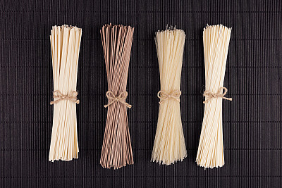 Different bundles raw noodles on black striped mat background with copy space, top view.
