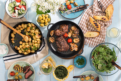 Grilled steak, grilled vegetables, potatoes, salad, different snacks and homemade lemonade on blue rustic wooden table