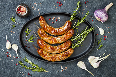 Grilled homemade rosemary sausages skewers on iron frying pan over rustic dark stone kitchen table. Top view, flat lay