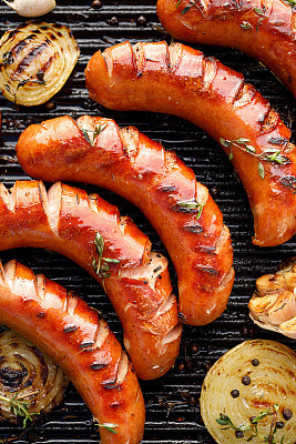 Grilled sausages with the addition of herbs and vegetables on the grill plate, top view.