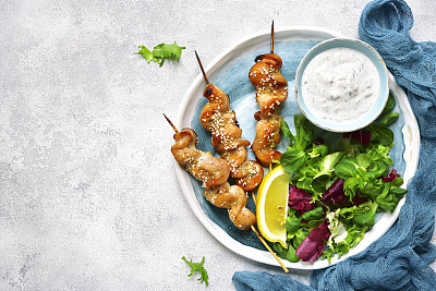 Grilled chiken breast on a skewers with mix of salad leaves and yogurt dip