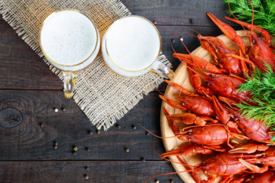 A  pile of tasty boiled crawfish on a round wooden tray and two mugs of cold beer on a dark background. Top view. Free space for an inscription.