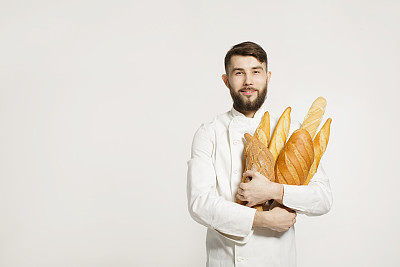 Handsome smiling baker in uniform holding baguettes with bread shelves on the white background. Handsome man holding warm bread in his hands on white background.