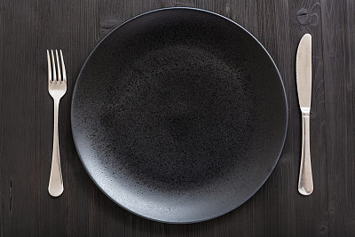 top view of black plate with knife, spoon on dark