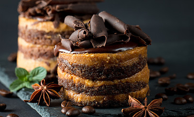 Chocolate cakes on black slatter board with mint, coffee beans on dark background, closeup photo. Fresh, tasty dessert food concept.