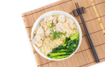 Wonton and egg noodle soup of Chinese Cantonese style for asian cuisine serving with Chinese cabbage (bog choy) and topped over bamboo plate mat isolated on white background, flat lay view