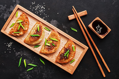 Asian fried dumplings with green onions, soy sauce, chopsticks on a black stone background. Top view, flat lay