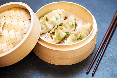 Steamed dumplings in bamboo steamer and chopsticks on a black concrete background